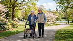 Elderly couple walking together outdoors using a rollator walker in a sunny park