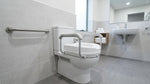 Senior safely using a raised toilet seat with armrests in a clean accessible bathroom