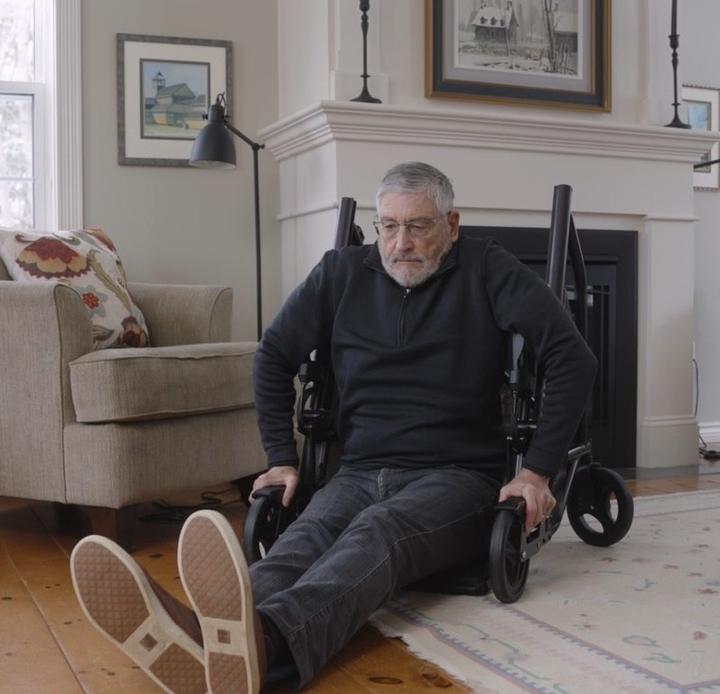 Senior man seated on the floor reaching for the RAYMEX Lift Quattro to self-recover after a fall