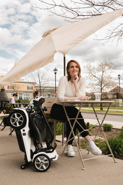 Heartway Transit 4 travel scooter folded beside a seated user outdoors